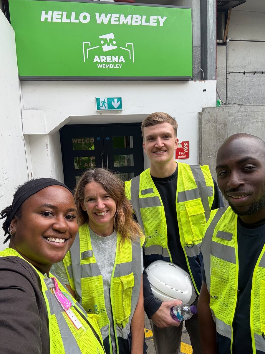 Rasheed and three crew in hi-vis vests outside the OVO Arena Wembley crew entrance, under a green Hello Wembley sign