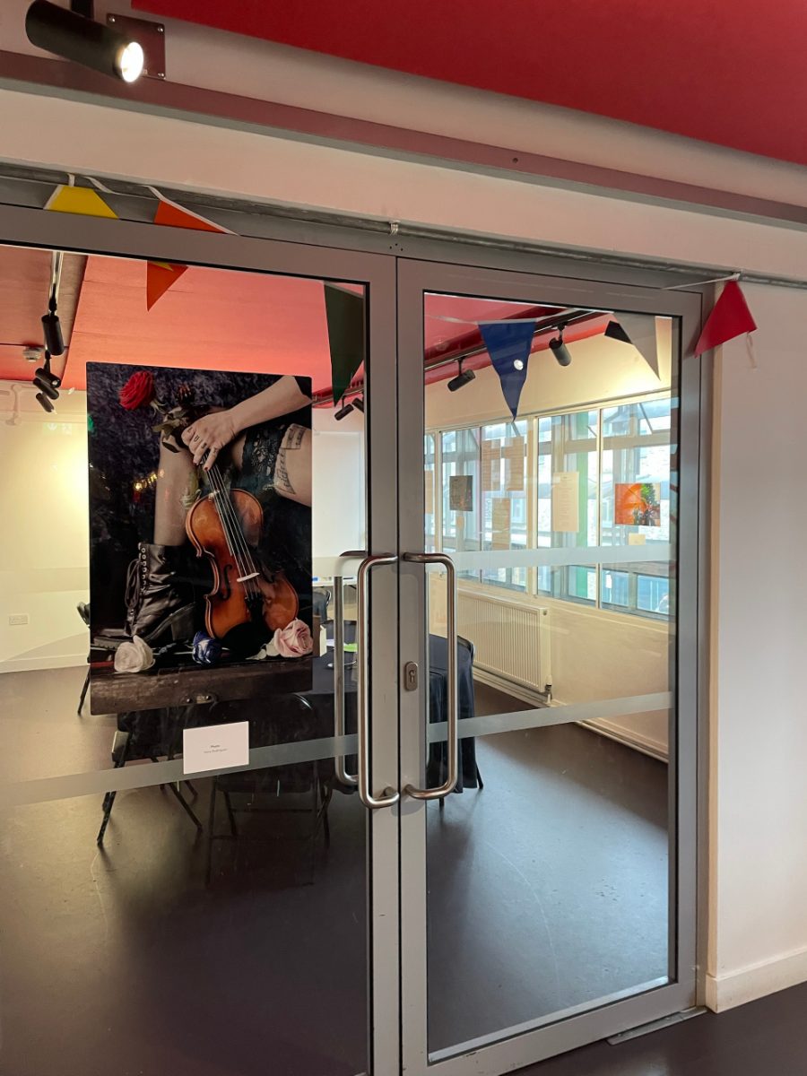 Gallery doors at the Sibling Art exhibition, with a photograph of a violin and roses hung inside